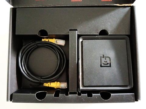 A square black networking device features two yellow Ethernet ports, a power switch