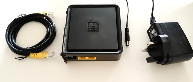 A square black networking device features two yellow Ethernet ports, a power switch