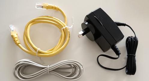A coiled yellow Ethernet cable, a bundled grey telephone wire, and a black AC power adapter