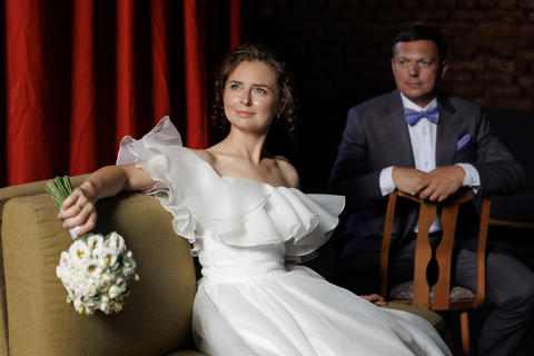 Bride and groom sit in chairs against a red curtain