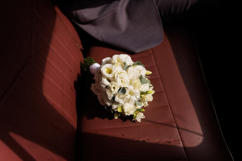 White rose bouquet rests on a red leather car seat