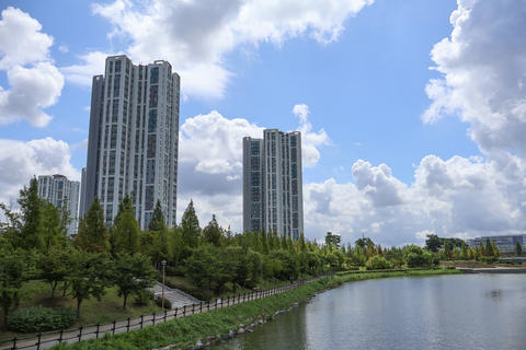 Modern high rise residential apartment buildings behind green park lake under cloudy blue sky