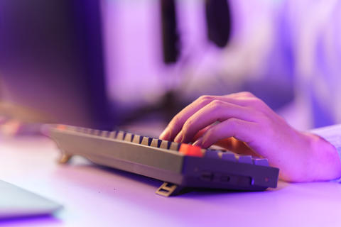 Cropped hand typing on mechanical keyboard with neon lighting for gaming and