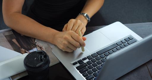 Hands using stylus on laptop at desk with coffee cup, notebook, and magazine