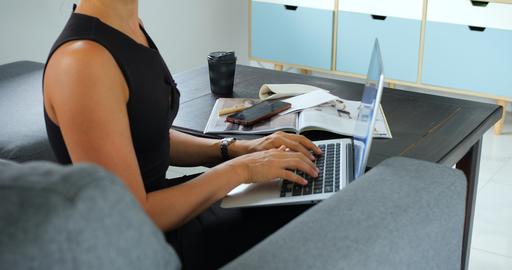 Woman typing on laptop beside notebook, smartphone, coffee cup, and open