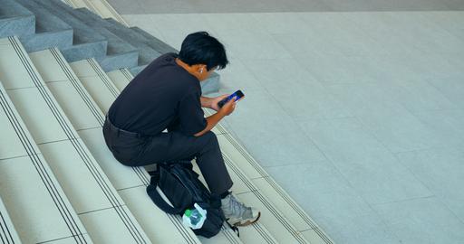Young man seated on indoor tiled stairs using smartphone, viewed from above
