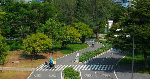 Cyclists riding on curving park path through lush green trees, one crossing