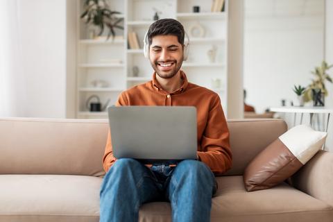 Happy Young Man Wearing Headphones Working On Laptop, Home Office Setting