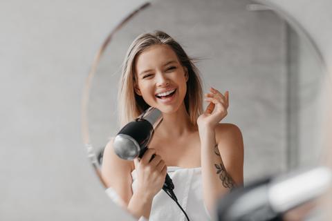 Happy Young Woman Drying Hair In Bathroom With Hairdryer, Indoor Wellness