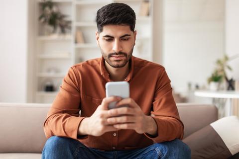 Focused Young Middle Eastern Man Texting On Smartphone At Home, Casual Setting