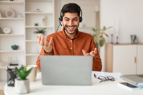 Happy Middle Eastern Man Video Calling At Home Office With Laptop And Headset