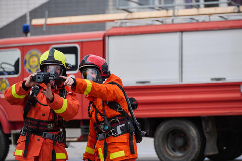 Firefighters In Protective Gear Using Thermal Camera By Red Fire Truck During