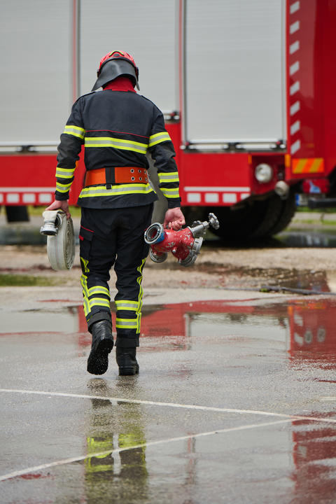 Firefighter Carrying Hose And Hydrant Toward Red Fire Truck On Wet Pavement