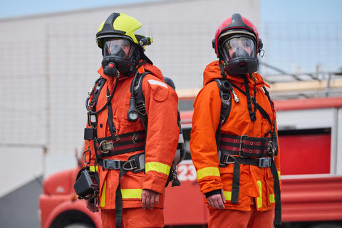 Two Firefighters in Orange Protective Gear With Breathing Masks Standing by Fire