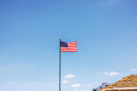 Close up view of American flag waving on tall flagpole above Miami Beach beneath clear sky. USA