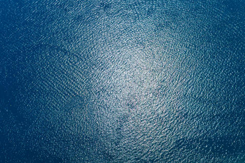 Aerial view of rippling blue water with sun reflections