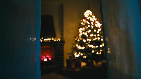 Behind the curtains of a window a bright Christmas tree in night room