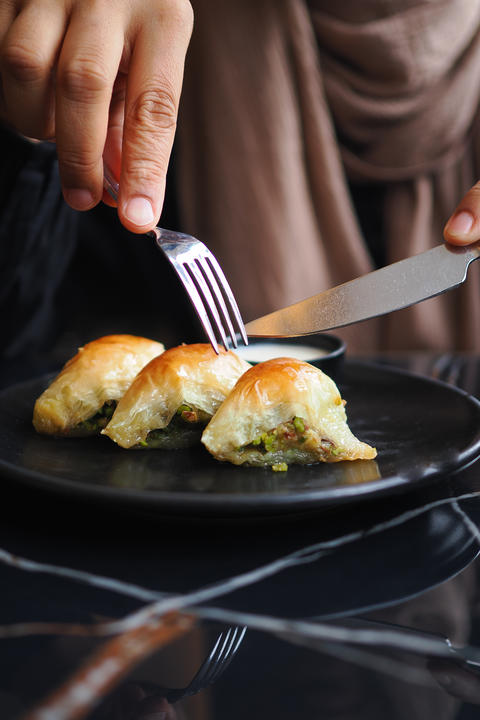 Person using fork and knife to cut baked pastry on a black plate