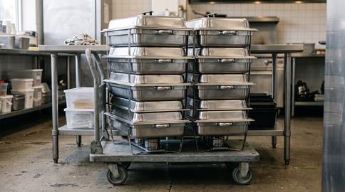Stacked stainless steel food pans on service cart in commercial kitchen