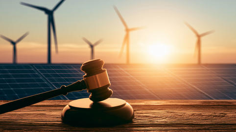 A judge’s gavel against the backdrop of solar panels and wind turbines at sunset