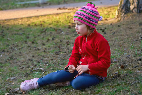 Pensive serious child girl sitting on ground in forest park