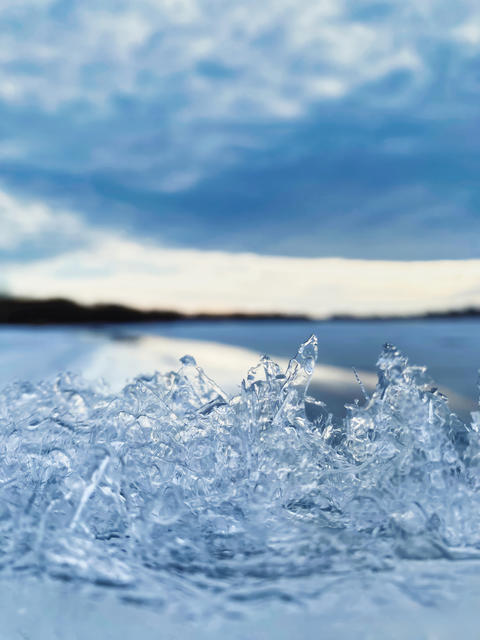 Close-up of transparent ice crystals on frozen lake under dramatic winter sky