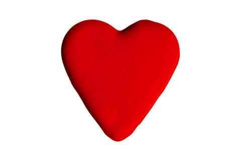 Red paint drop forming heart shape on white background surface