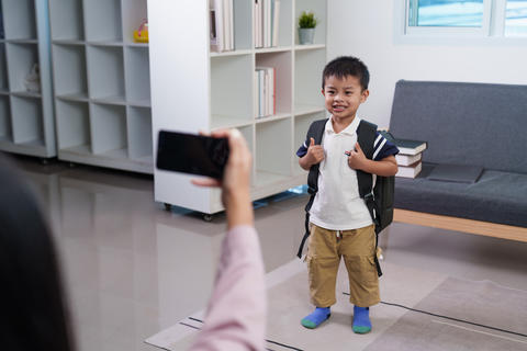 Mother taking photo of young son with smartphone on first day of school