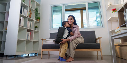 Asian mother hugging son with backpack at home for back to school preparation