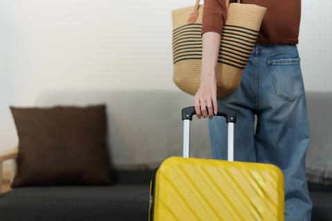 Cropped view of traveler holding yellow suitcase handle ready for trip departure