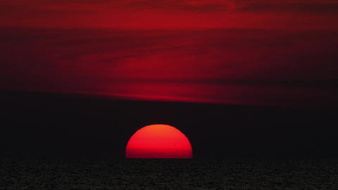 Dramatic red sun setting over dark ocean horizon at dusk