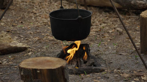 Bright flames heat cast iron pot on tripod over forest campfire