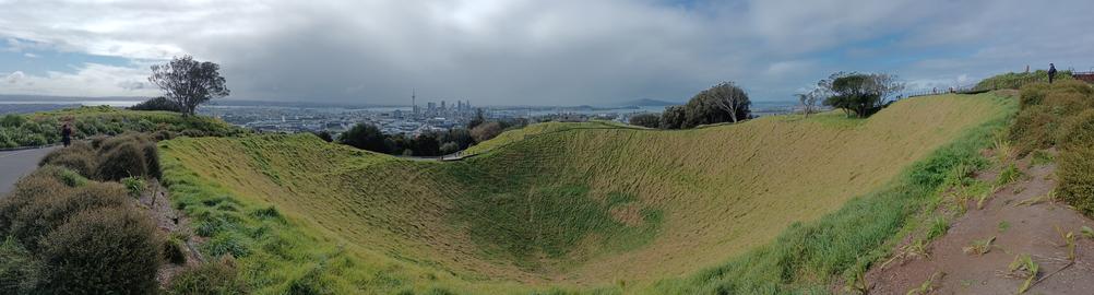 Panoramic view of Auckland spreading across rolling volcanic hills, with green grass