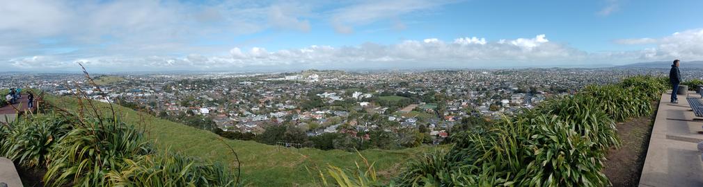 Panoramic view of Auckland spreading across rolling volcanic hills, with green grass