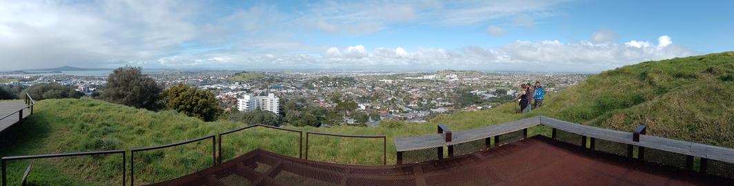 Panoramic view of Auckland spreading across rolling volcanic hills, with green grass