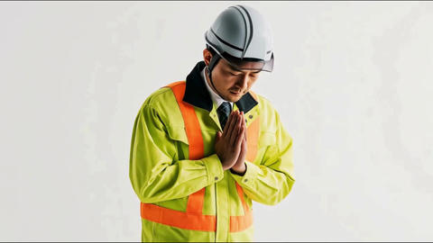 Male construction worker in a helmet and work clothes, bowing with hands pressed