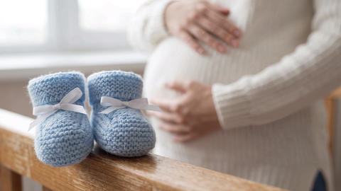 Pregnant Woman Holding Her Belly with Blue Baby Booties on Foreground