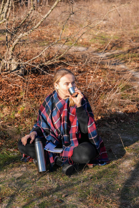 Young woman pouring hot drink from thermos during outdoor break