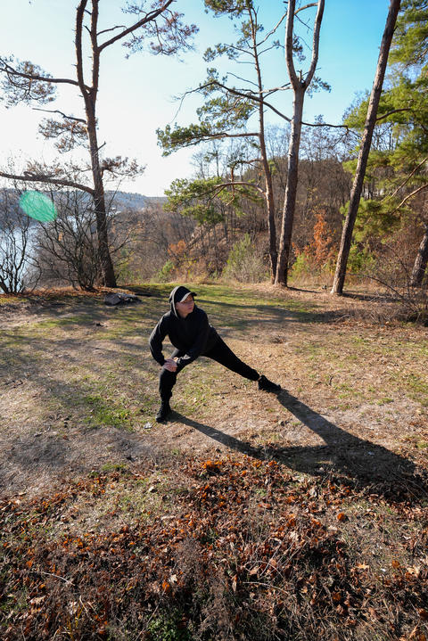 Young woman dressed in black sportswear stretches in side lunge position on