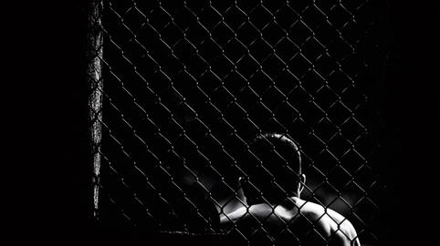 Fighter standing behind chain link fence in cage