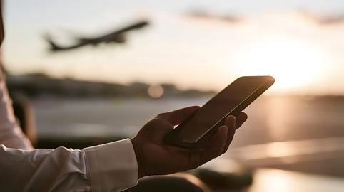 Person holding smartphone watching airplane taking off at sunset
