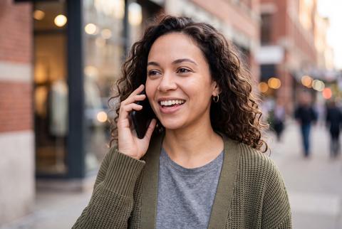 Smiling Woman Talking on Smartphone While Walking on Urban Street