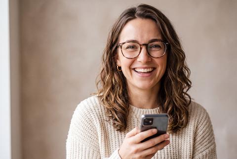 Smiling Woman Holding Smartphone Wearing Glasses in Casual Interior