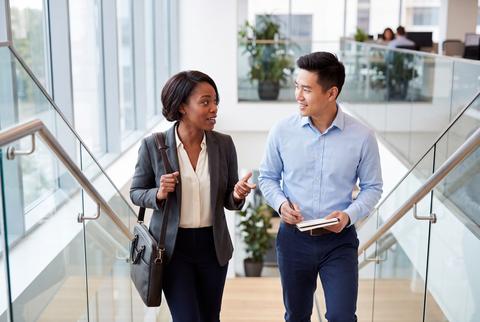 Colleagues walking up stairs and discussing work in modern office building