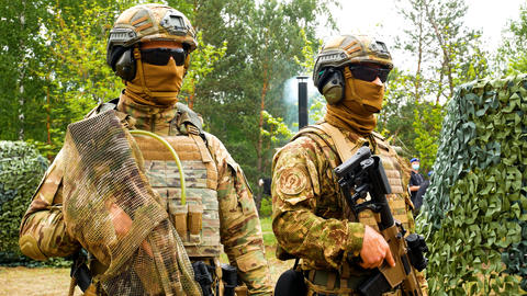 Two soldiers in military uniforms, body armor, helmets, with weapons stand near