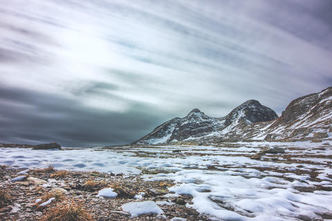 Snow covered rocky landscape with cloudy sky and mountain peaks