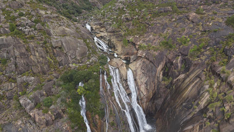 Aerial view of waterfall flowing through dramatic rocky gorge and forest