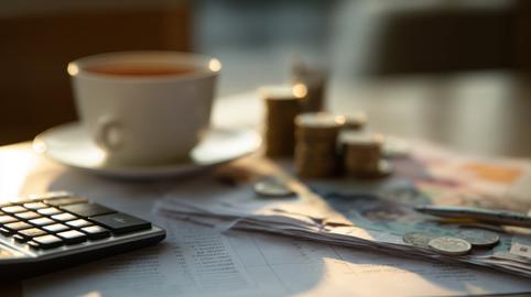 Calculator, financial documents and scattered coins beside a coffee cup on a work desk