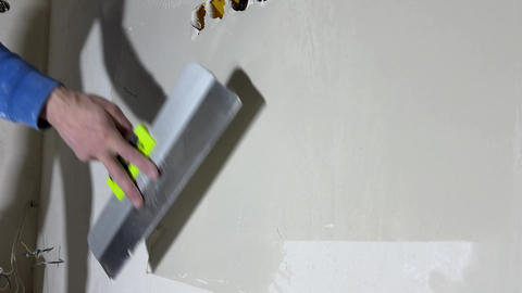 Male hand of worker apply plaster with wide metal spatula to wall