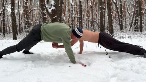Two male athletes performing atypical partner push-ups on deep snow in winter forest